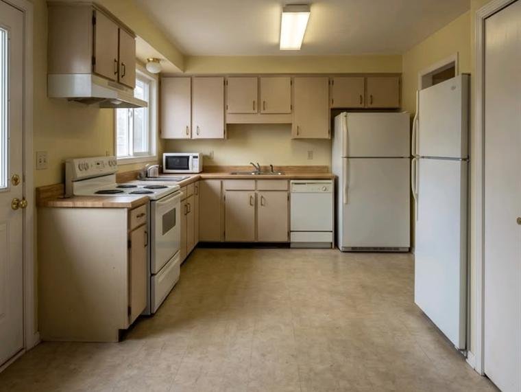 Cramped kitchen with pale laminate cabinets, a white fridge and sheet vinyl flooring, before renovation.