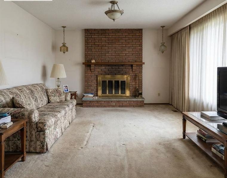 Living room with a floor-to-ceiling red brick fireplace, brass doors and worn carpet, before renovation.