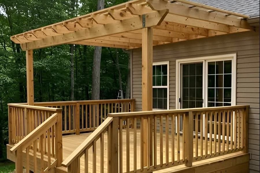 A cedar deck with a pergola, railings and steps attached to the rear of a house.