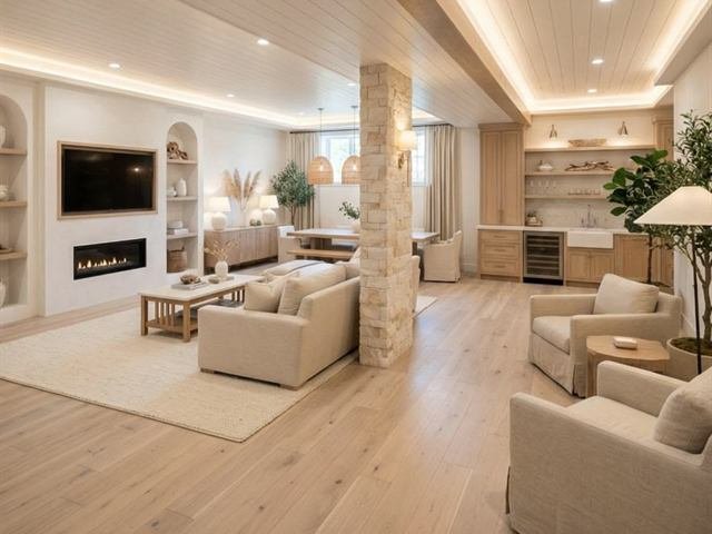 A finished basement living space with built-in shelving, a linear fireplace and a wet bar.